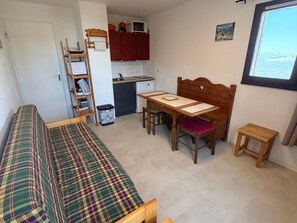 Ein gemütlicher Raum mit Bett, Esstisch mit Stühlen, einer kleinen Küchenzeile und einem Fenster.