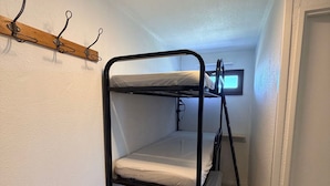 A bunk bed with a television on the upper bunk, a wooden shelf, and a small wooden table.