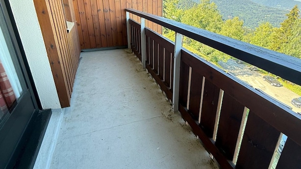 A balcony with a wooden floor and railing, overlooking a mountainous landscape.