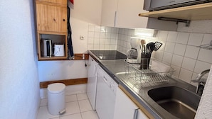 A compact kitchen with a dishwasher, sink, and a wooden shelf with a kettle and toaster.