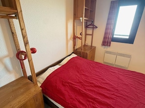 Ein Schlafzimmer mit einem Holzbett, einem roten Überwurf, einem Kleiderschrank, einem Spiegel und einem Fenster mit Vorhängen.