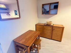 Ein Holzesstisch mit Bänken, ein Schrank mit Schubladen, eine Pendelleuchte und ein gerahmtes Bild an der Wand.