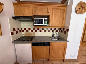 A compact kitchen with wooden cabinets, a built-in microwave, a dishwasher, and a small refrigerator. - 3-room luxury apartment at the foot of the slopes with private parking (Les Adrets-Prapoutel)