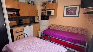 A compact room with a kitchenette, a bed with a floral-patterned headboard, and a television mounted on the wall. - Studio cabin at the foot of the slopes, 2 rooms (Les Adrets-Prapoutel)