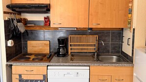 A compact kitchen with wooden cabinets, a built-in stove, a coffee maker, and a dishwasher. - Studio cabin at the foot of the slopes, 2 rooms (Les Adrets-Prapoutel)