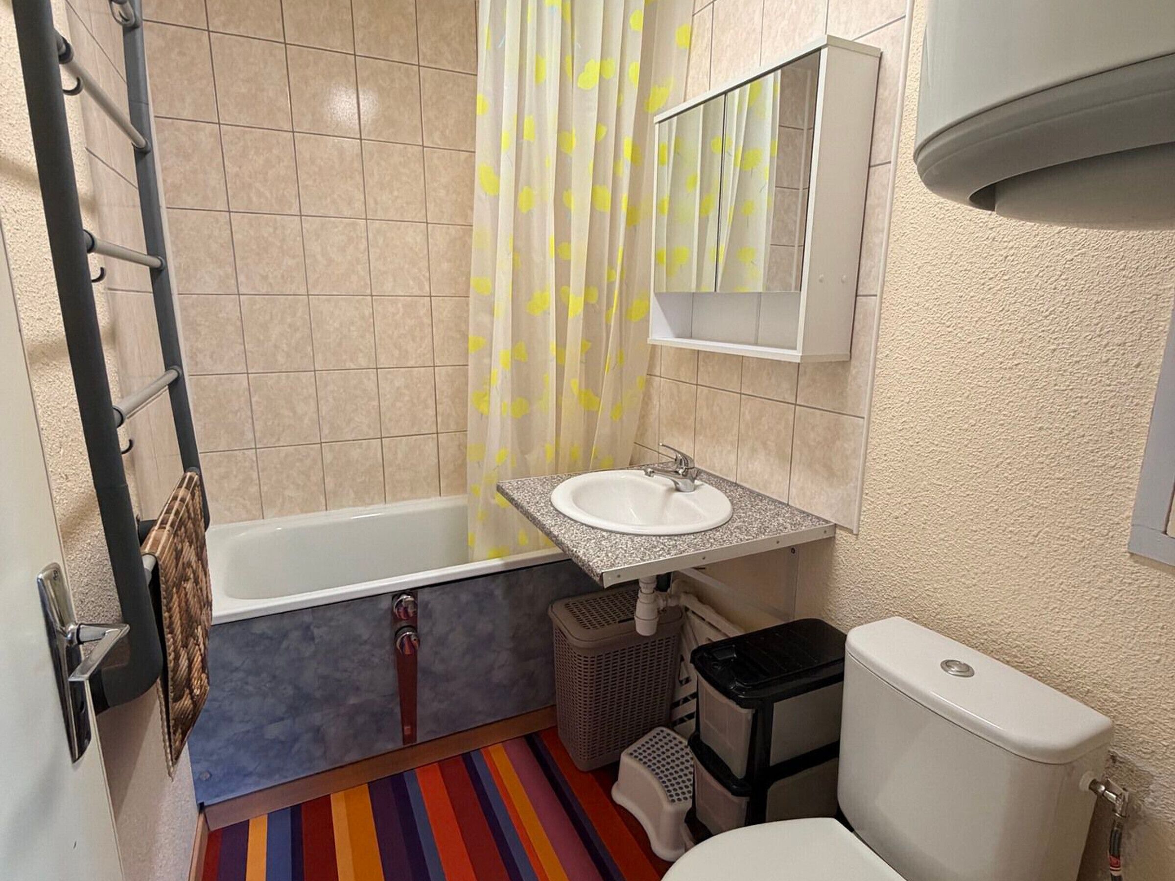A bathroom with a bathtub, a sink, a toilet, and a shower curtain with yellow patterns.