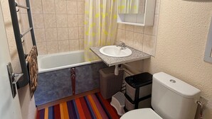 A bathroom with a bathtub, a sink, a toilet, and a shower curtain with yellow patterns. - Studio cabin at the foot of the slopes, 2 rooms (Les Adrets-Prapoutel)