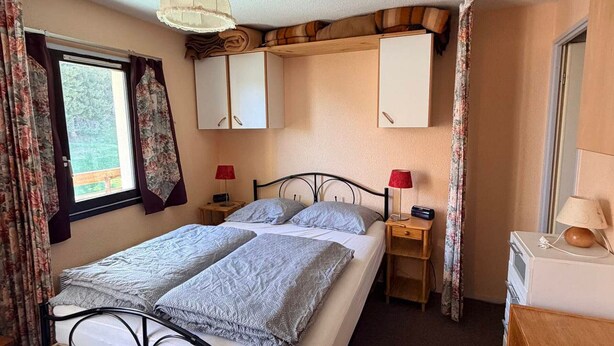 A bedroom with a bed, two bedside tables, a lamp, a wardrobe, and a window with curtains. - Studio cabin at the foot of the slopes, 2 rooms (Les Adrets-Prapoutel)