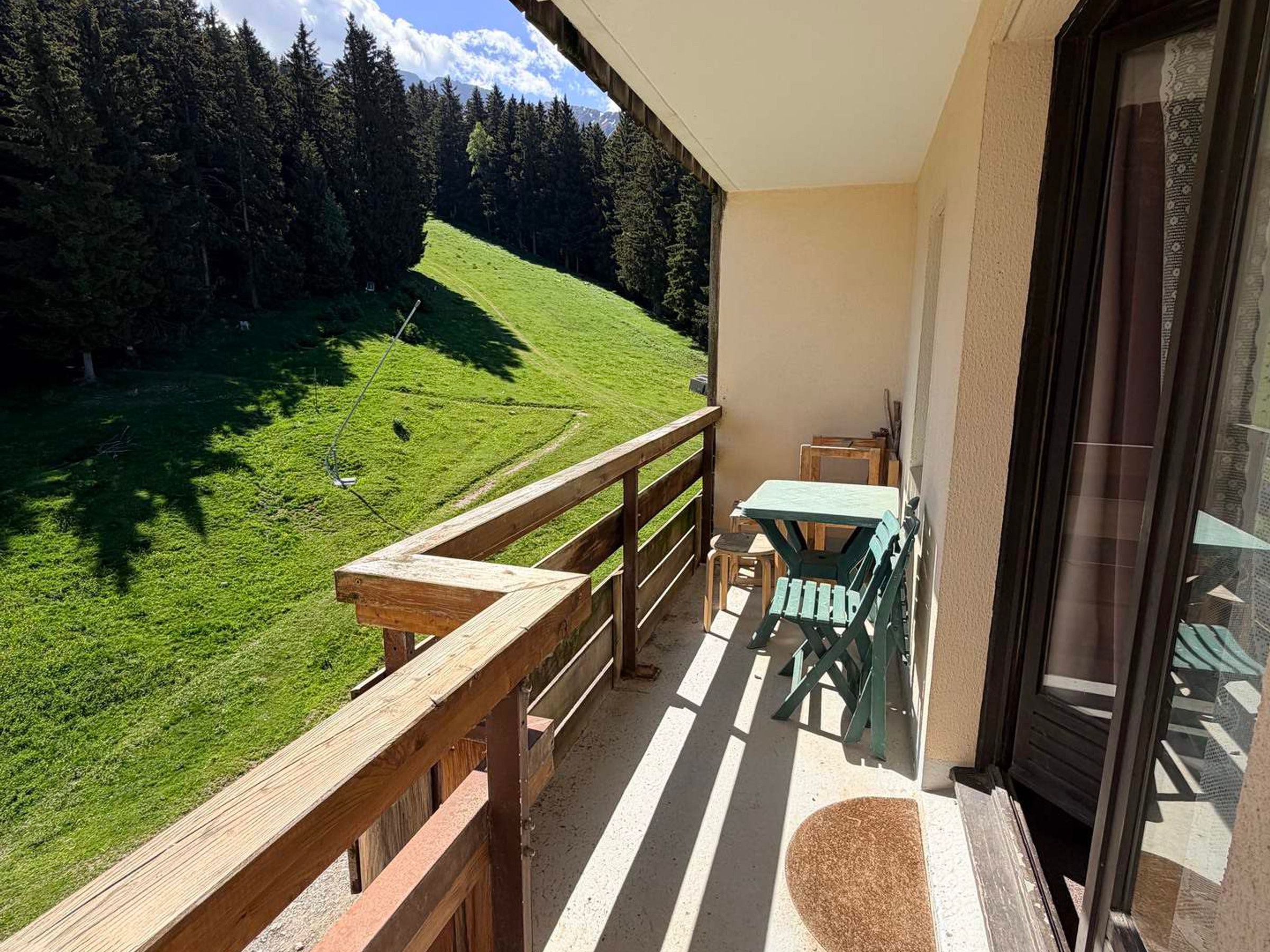 Ein Balkon mit Holzwertung, Tisch und Stühlen mit Blick auf eine grüne Landschaft mit Bäumen und einem Hügel.