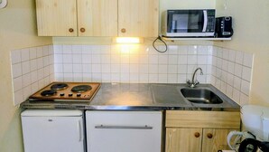 Una cocina compacta con armarios de madera, microondas, estufa, lavabo y refrigerador pequeño.