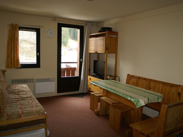 Een kleine kamer met een bed, een bureau, een televisie en een raam met gordijnen.