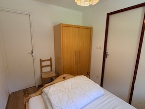 A bedroom with a bed, a wooden wardrobe, a chair, and a door.