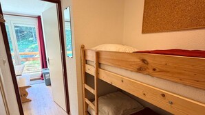 A bunk bed with a red blanket, a wooden headboard, and a small storage drawer.