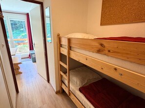 A bunk bed with a red blanket, a wooden headboard, and a small storage drawer.