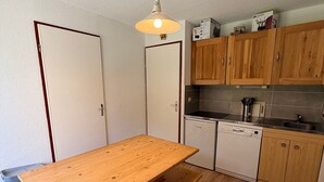 A compact kitchen with wooden cabinets, a built-in dishwasher, and a wooden table.