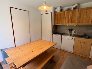 A compact kitchen with wooden cabinets, a built-in dishwasher, and a wooden table.