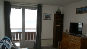 Een woonkamer met een bank, een televisie, houten kasten en een balkon met gordijnen.