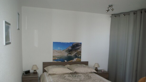 Een slaapkamer met een bed, twee nachtkastjes, een bedlamp, een foto aan de muur en een raam met gordijnen.