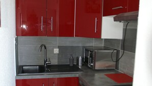 Een keuken met rode kastjes, een roestvrijstalen spoelbak, een broodrooster en een magnetron.