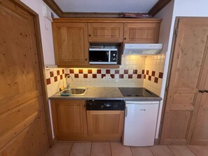 Una cucina compatta con mobili in legno, un forno a microonde, una lavastoviglie e un frigorifero.