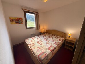 Una camera da letto con un letto, due lampade ai comodini, una finestra con tende, un termosifone e un quadro appeso al muro.