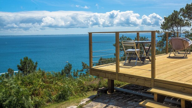 Une terrasse en bois avec des sièges extérieurs offrant une vue sur la côte.