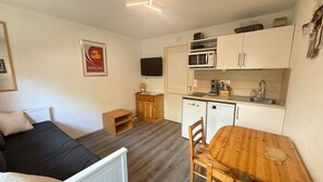 A compact room with a bed, a small kitchenette, a wooden table, and a television.