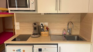 A compact kitchenette with a microwave, coffee machine, sink, and a small refrigerator.