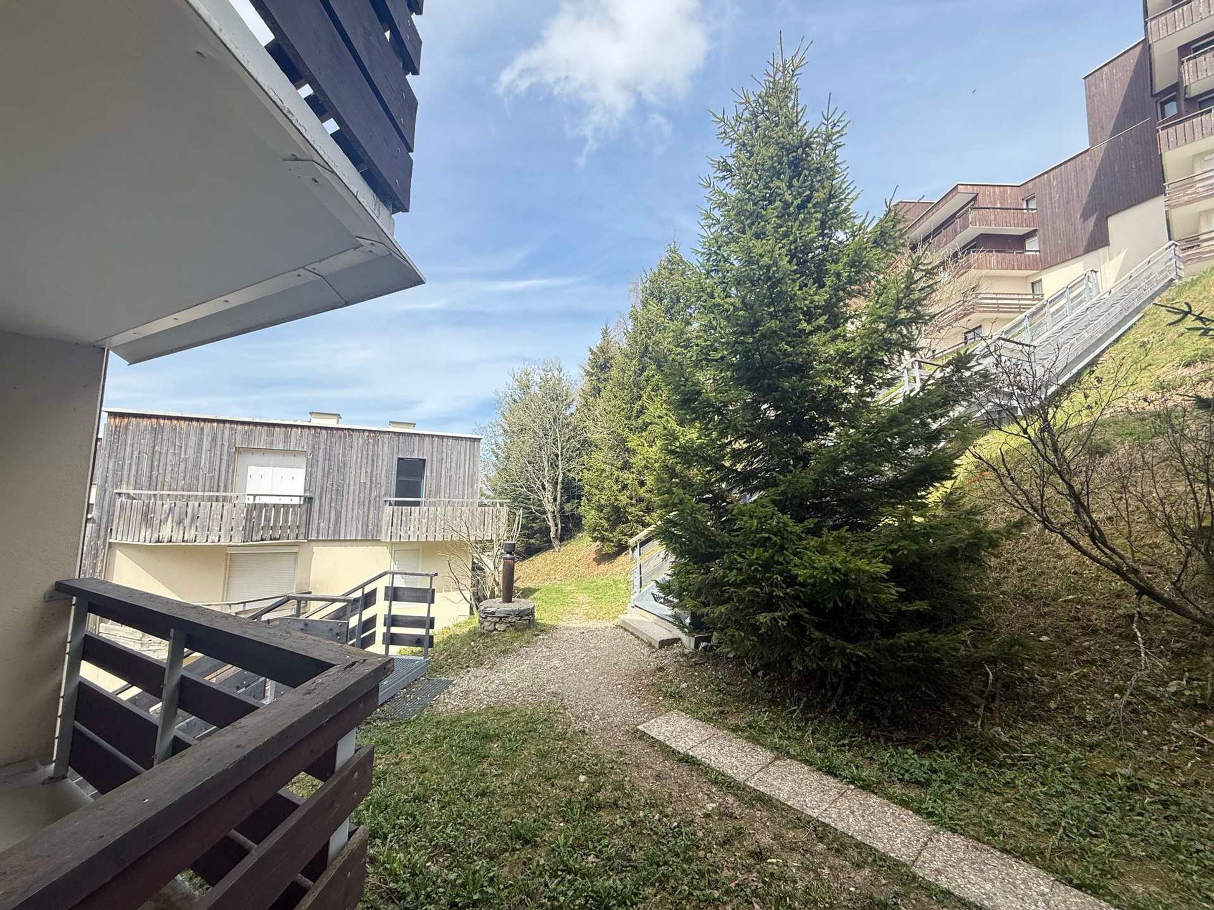 A residential building with a balcony, a gravel pathway, and a large evergreen tree.