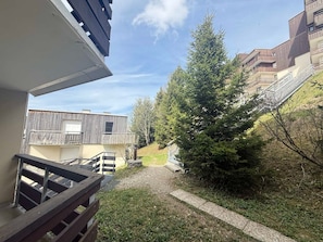 Um edifício residencial com varanda, um caminho de cascalho e uma grande árvore perene.