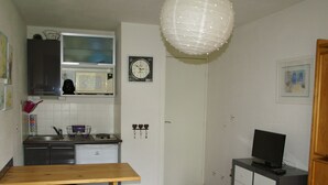 A compact kitchen with a microwave, stove, and sink. There is a wooden table with benches, a small cabinet, and a television on a stand.