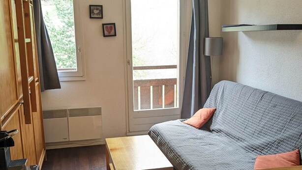 A cozy room with a grey sofa, a wooden table, and a window with curtains.