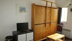 A room with a wooden wardrobe, a desk, a chair, and a television.