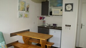 A compact kitchen with a wooden table and bench, a microwave, and a clock on the wall.