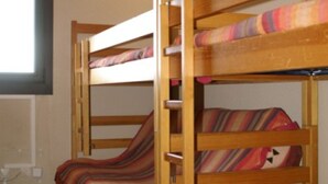 Een stapelbed met gestreepte lakens in een kamer met een raam en een radiator.