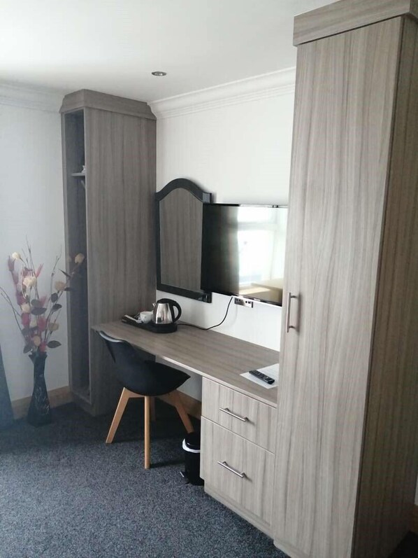 A compact hotel room with a wooden desk, a chair, a television, and a wardrobe. - The Reveller Lodgings (Donegal)