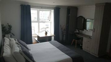 A hotel room with a bed, a desk, a chair, a television, and a wardrobe.