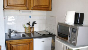 A compact kitchen with wooden cabinets, a sink, a small refrigerator, a microwave, and a green-tiled table.
