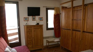A bedroom with a bed, wooden wardrobe, a television, and a window with curtains.