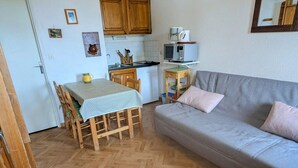 A compact living space with a dining table, wooden chairs, a sofa, a kitchenette with a microwave, and a small cabinet.