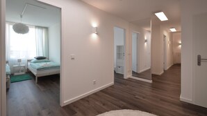 A modern hotel room with a wooden floor, a bed with a green bedspread, a nightstand, and a window with curtains. - 3 Bathroom - Rhapsody In Roof - Penthouse (München)