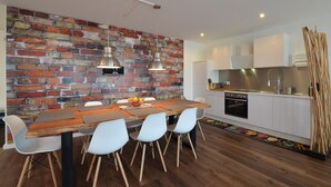 A modern kitchen with a brick wall backsplash, white cabinetry, and a wooden dining table with chairs. - 3 Bathroom - Rhapsody In Roof - Penthouse (München)