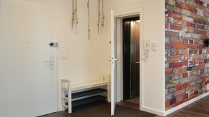 A hallway with a white door, a bench, a staircase, and a brick wall. - 3 Bathroom - Rhapsody In Roof - Penthouse (München)