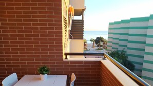 Un balcon avec une table et des chaises blanches, une plante en pot et une vue sur la mer et les palmiers.