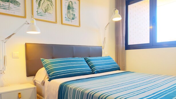 Une chambre à coucher avec un lit, deux tables de chevet, une commode et une fenêtre avec des rideaux.