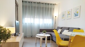 Un salon moderne avec un canapé, des fauteuils jaunes, une petite table et un téléviseur.