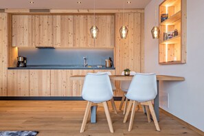 A modern kitchen with wooden cabinetry, pendant lights, a dining table with chairs, and a small shelf with decorative items. - Beautiful Apartment “Aura Chalets Nr 1” with Mountain View, Wi-Fi & Garden (Kastelruth)