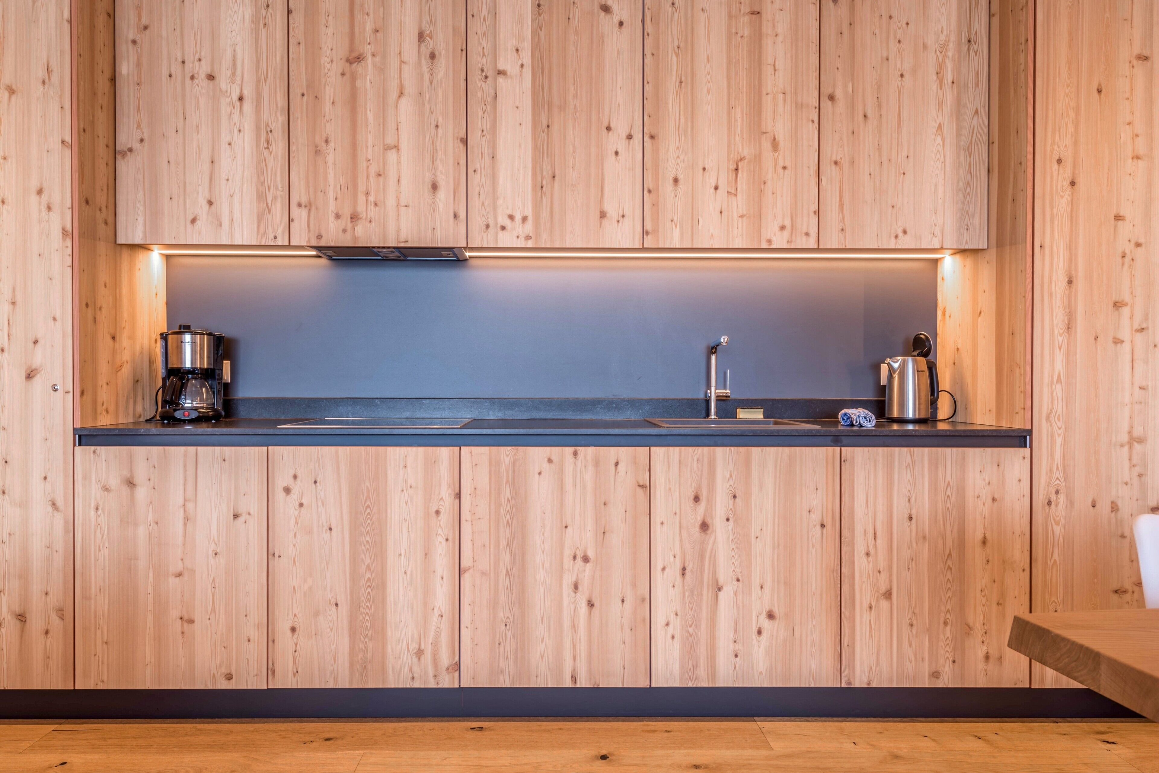 Una cocina moderna con armarios de madera, encimera negra, cafetera, hervidor y lavabo.
