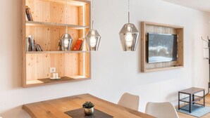 Un comedor moderno con una mesa de madera, dos lámparas colgantes, una estantería y un cuadro en la pared.