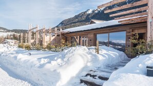 Une cabane en bois dotée de grandes fenêtres, d’un toit recouvert de neige et surplombant un paysage montagneux.